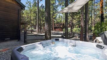 Un bain à remous entouré d’arbres, un chalet en bois et un espace abrité.