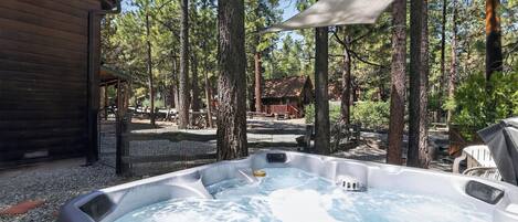 Un jacuzzi rodeado de árboles, una cabaña de madera y un área cubierta.