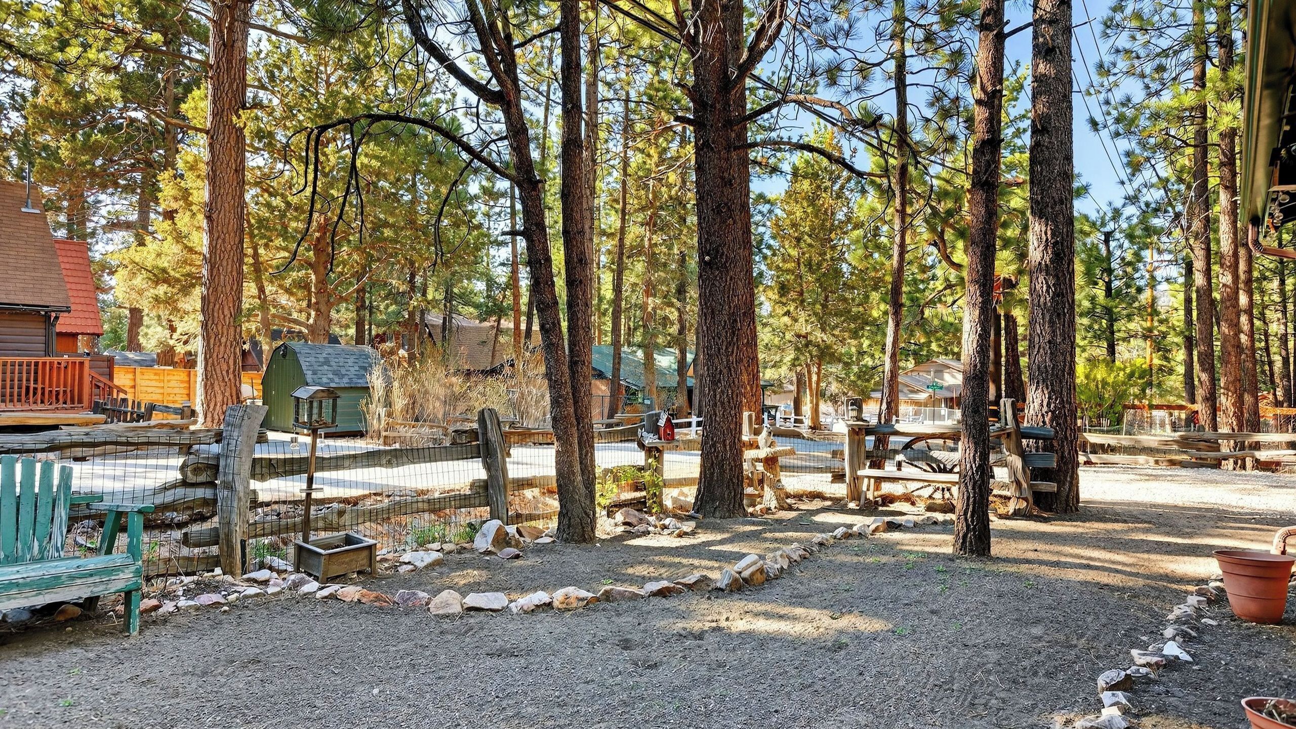 A campground with tents, a wooden deck, and a fenced area with a bench and a bird feeder.