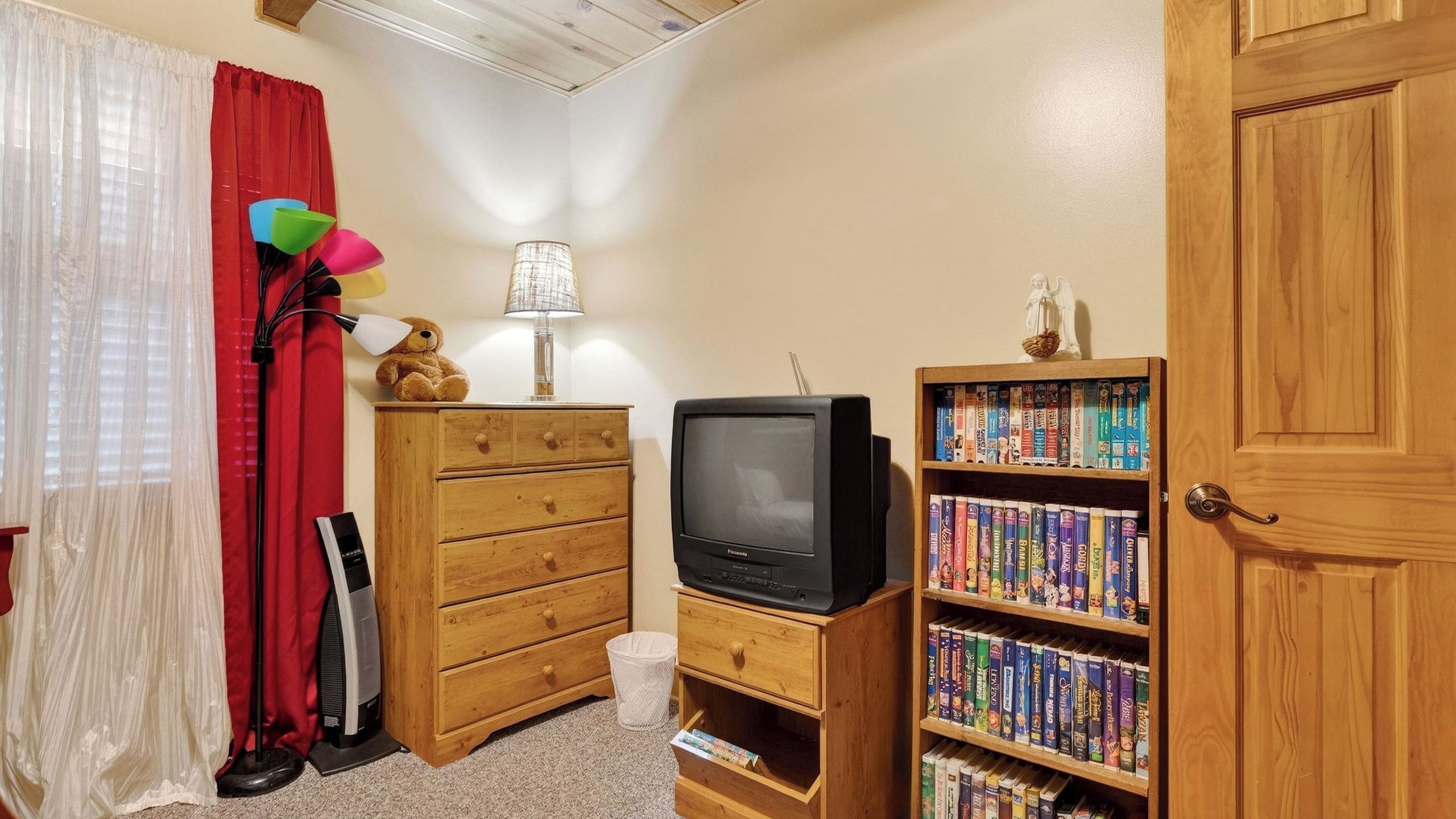 A room with a wooden dresser, a television, a bookshelf, and a red curtain.