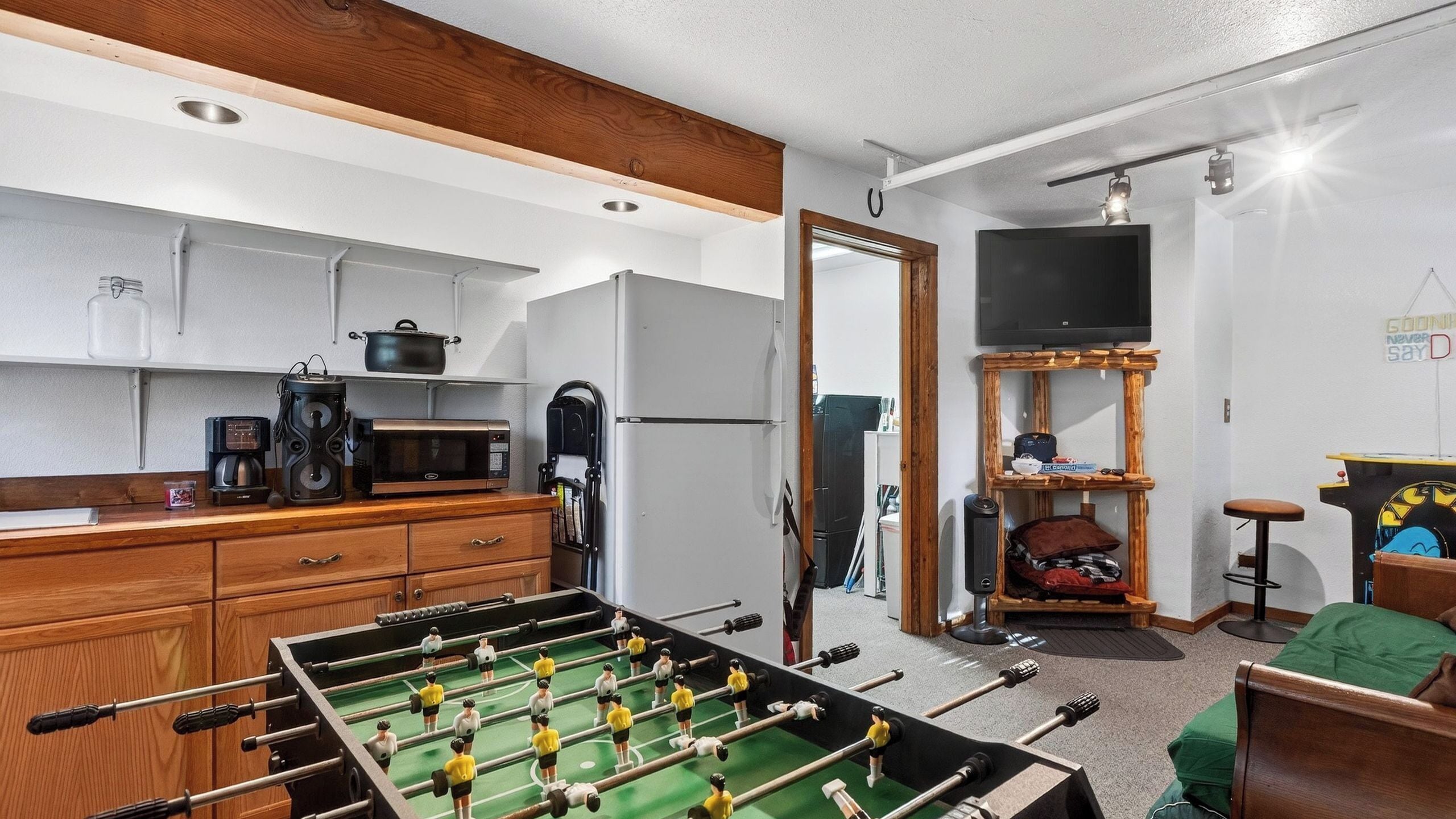 Un espace de vie compact comprenant un coin cuisine, une table de baby-foot, un téléviseur et un petit coin salon.