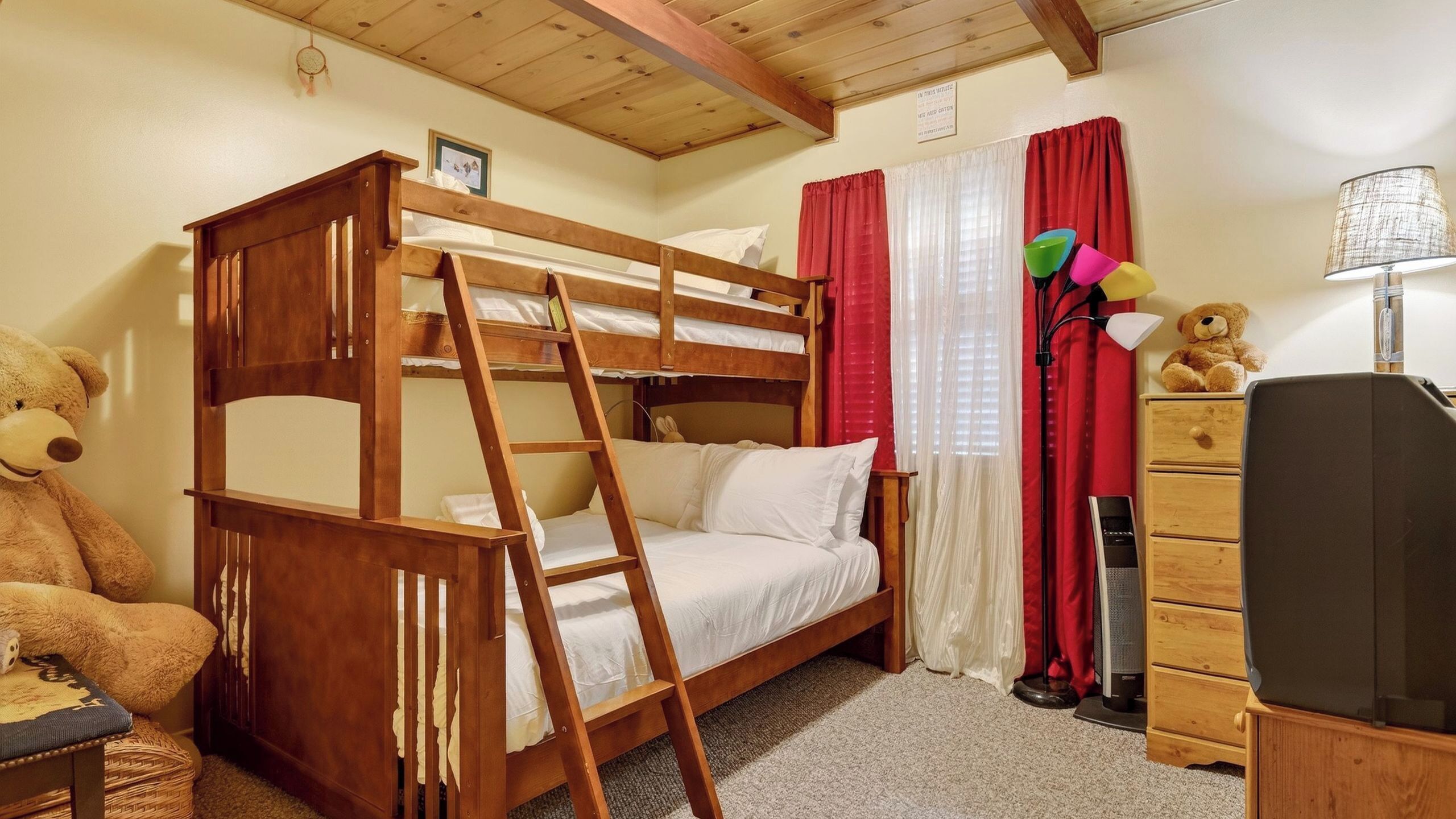 A bunk bed room with a ladder, a teddy bear, a dresser, and a lamp.
