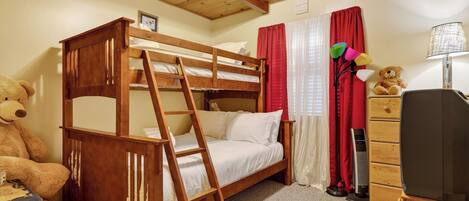 A bunk bed room with a ladder, a teddy bear, a dresser, and a lamp.