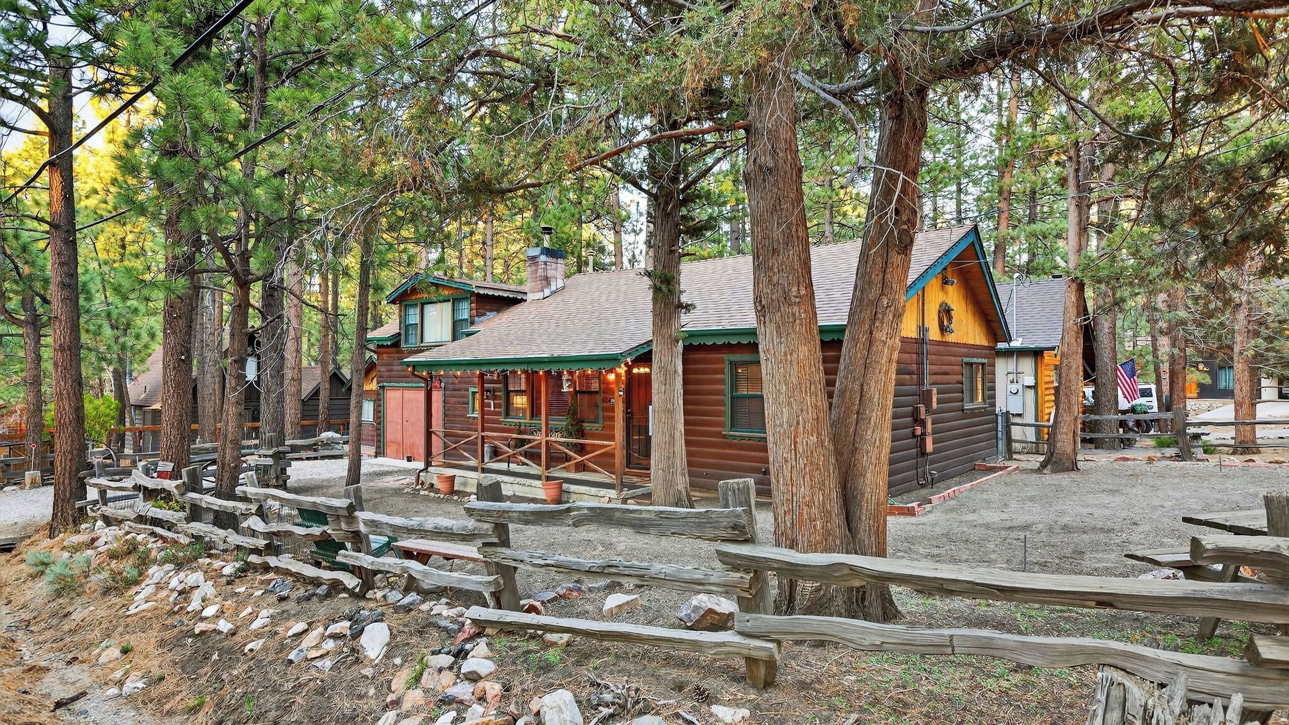 Un chalet rustique en rondins de bois, doté d’un porche et entouré de grands arbres.