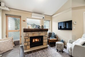 Una sala de estar con chimenea de piedra, un televisor de pantalla plana en la pared y un ventanal grande.