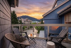 Ein Balkon mit zwei Adirondack-Stühlen, einem kleinen runden Tisch und einem Getränk.