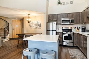 Una cocina moderna con electrodomésticos de acero inoxidable, un comedor con mesa y sillas, y una escalera que sube a otro nivel.
