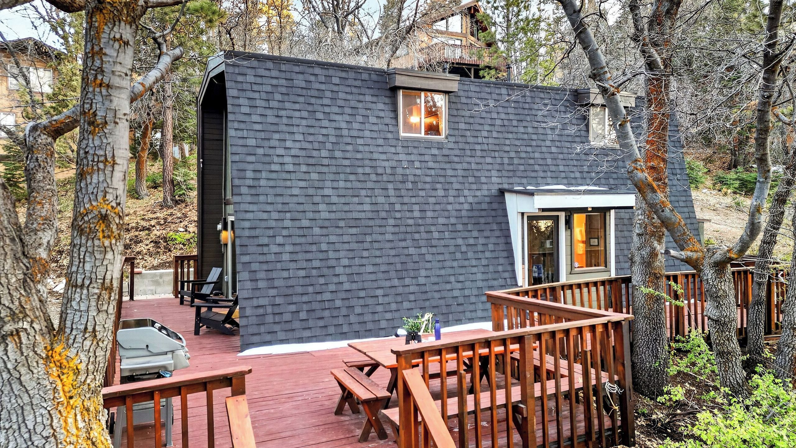 Une cabane moderne à l’extérieur sombre, dotée d’une terrasse avec des meubles en bois et d’un garage apparent.