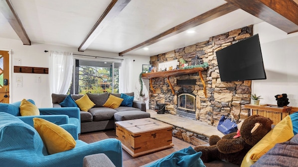 Ein Wohnzimmer mit Kamin aus Stein, einer Sofagarnitur, einem Fernseher und einer Bärenstatue.