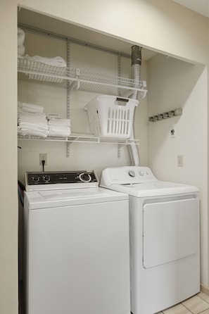 A laundry room with a front-loading washer and dryer, shelves with folded towels, and a laundry basket. - Peaceful Cabin w/ Hot Tub Near Mt Rainier (Packwood)