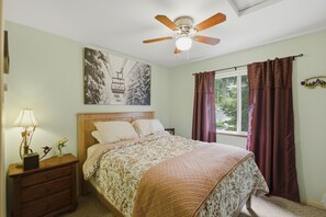 A bedroom with a bed, a nightstand, a lamp, a ceiling fan, a window with curtains, and a wall-mounted picture. - Peaceful Cabin w/ Hot Tub Near Mt Rainier (Packwood)