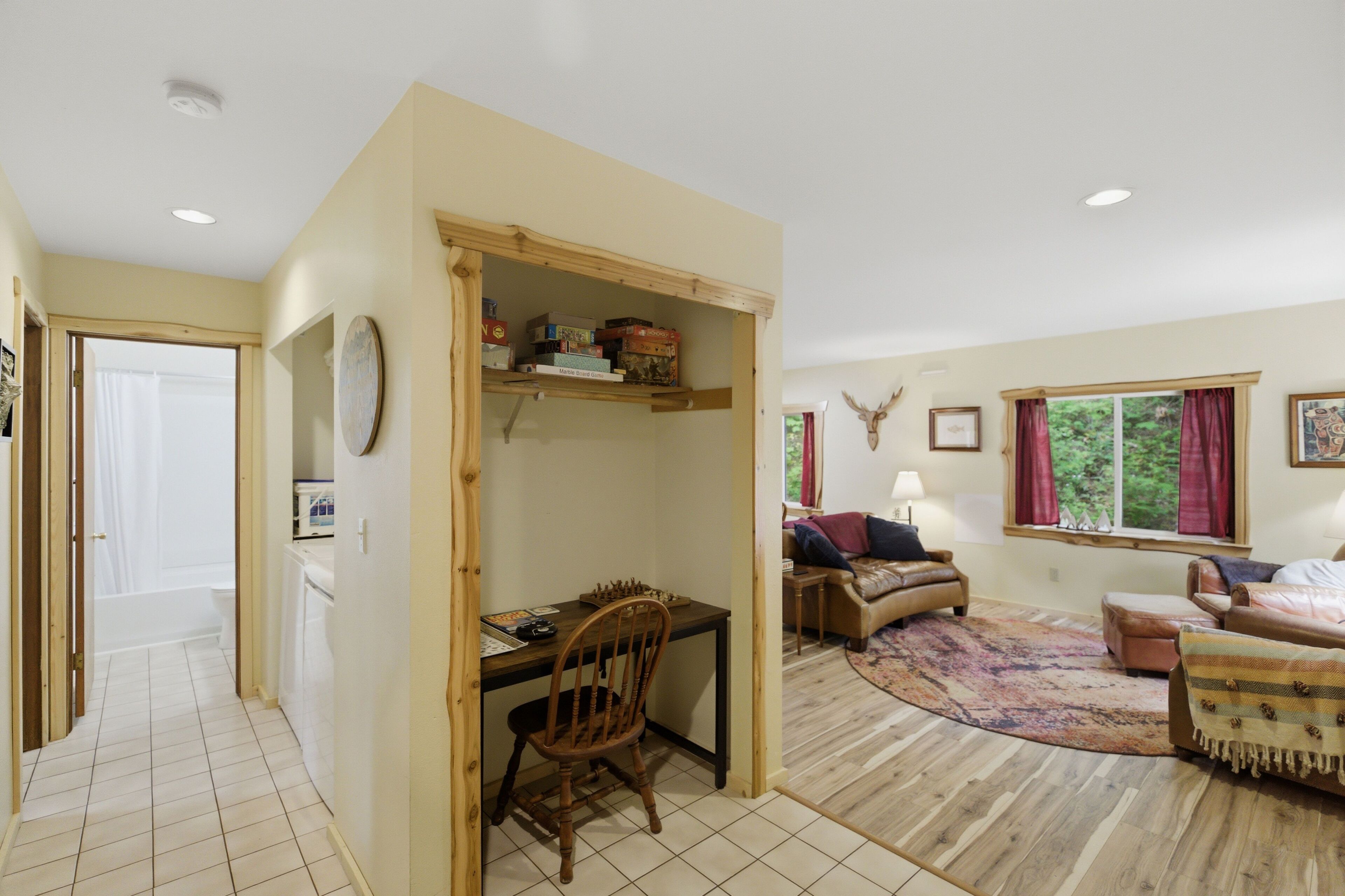A room with a wooden desk, a chair, a sofa, a rug, and a window with curtains.