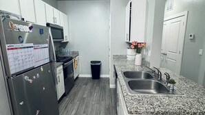 Eine moderne Küche mit weißen Schränken, einem Edelstahl-Kühlschrank, Granit-Arbeitsplatten und einem eingebauten Backofen.