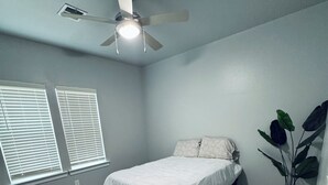 Ein Schlafzimmer mit einem Bett, einem Deckenventilator und einer Topfpflanze.