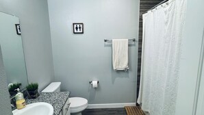 Ein modernes Badezimmer mit einer Granittafel, einem weißen Waschbecken, einer Toilette und einer Duschvorhang.