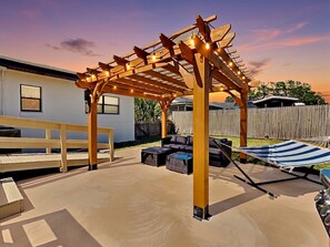 Uma área de varanda coberta com pérgola de madeira, assentos externos e uma rede.
