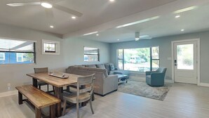 Un salón espacioso con comedor, ventilador de techo y ventanas grandes.