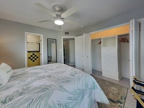 Quarto com cama, ventoinha no teto, guarda-roupa e espelho.