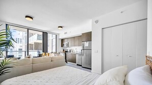 Een moderne slaapkamer met een groot bed, een slaapbank en uitzicht op de stad door grote ramen.