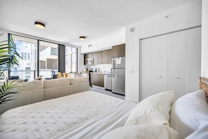Ein modernes Schlafzimmer mit einem großen Bett, einer Sitzecke und Blick auf die Stadt durch große Fenster.