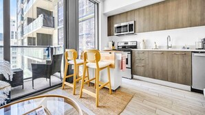 Een moderne keuken met een magnetron, fornuis en spoelbak. Er staan twee houten stoelen bij een glazen tafel.
