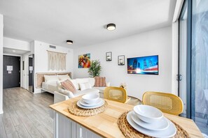 Ein modernes Wohnzimmer mit einer Couch, einem Esstisch und Stühlen. Es gibt ein großes Fenster, eine Pflanze und Kunstwerke an den Wänden.