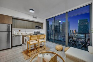 Une cuisine moderne avec un coin repas, de grandes fenêtres offrant une vue sur la ville et un balcon aménagé avec des sièges.