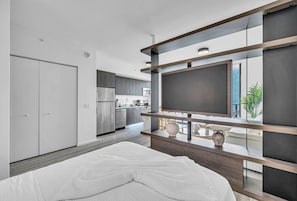 Une chambre à coucher moderne avec un lit, une télévision et une cuisine en arrière-plan.