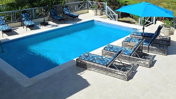 Una piscina con sillas de descanso y sombrillas, un edificio pequeño y vistas al océano.