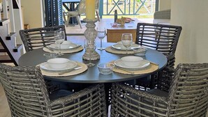 Comedor con una mesa redonda, sillas de mimbre y vista a palmeras a través de un ventanal.