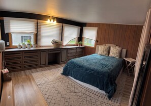 Un dormitorio con cama, escritorio con cesta y ventana con persianas.