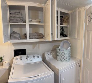 Un espace buanderie comprenant un lave-linge et un sèche-linge à chargement frontal, une étagère avec des serviettes pliées et un panier posé sur le sèche-linge.
