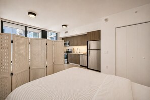Quarto moderno com uma cama grande, uma kitchenette com frigorífico e micro-ondas, e vista pela janela.