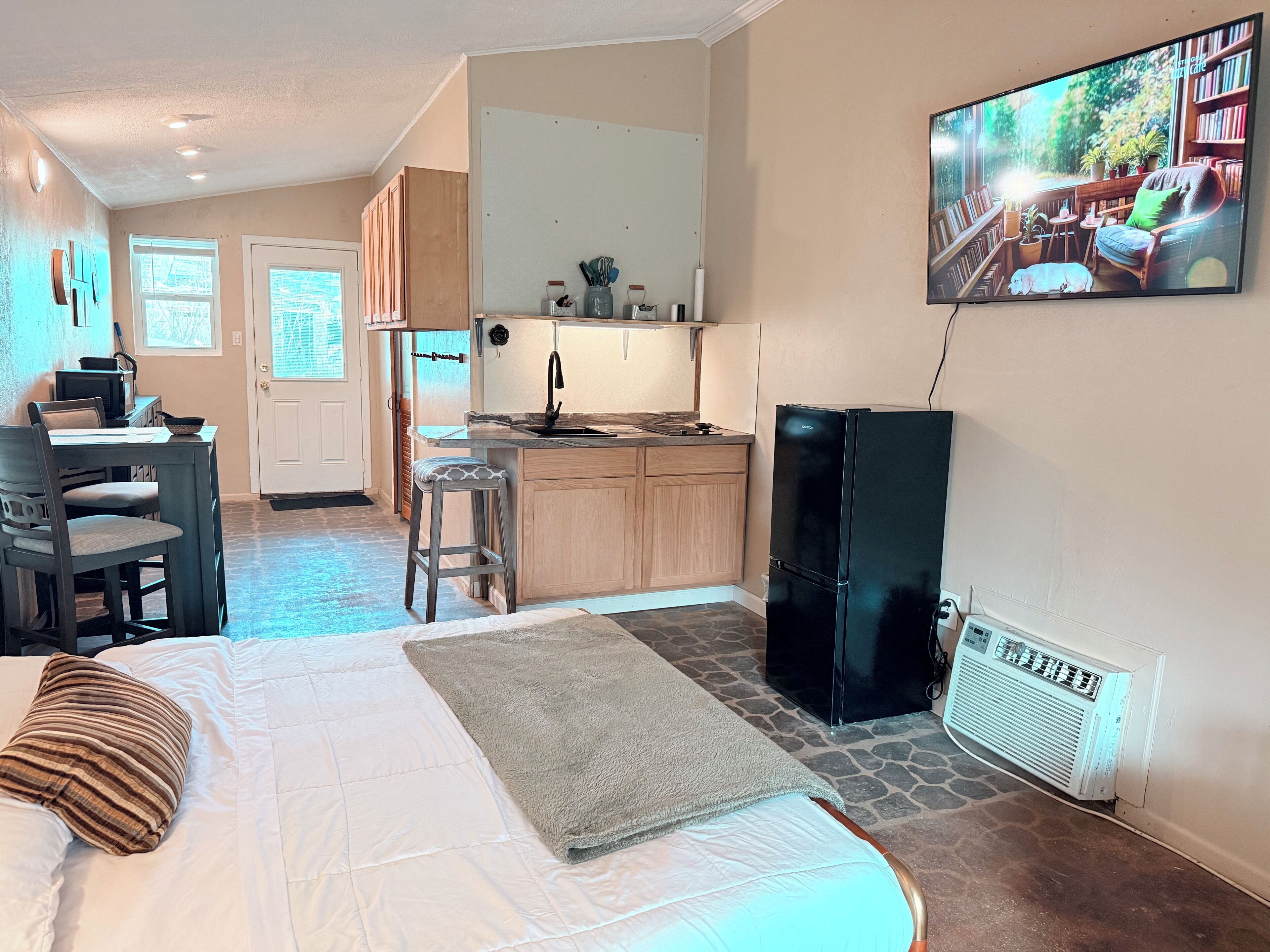 Un espace de vie compact comprenant un coin cuisine, un lit avec vue et un téléviseur diffusant des images d'un paysage extérieur.