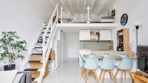 Un apartamento moderno estilo loft con zona de comedor, cocina y una escalera que sube a un dormitorio en un entrepiso.
