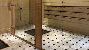 Un vestíbulo de hotel con un muro espejado, una columna de madera, suelo de baldosas y un conjunto de taquillas.