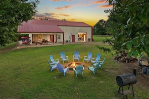 A barn with a fire pit and chairs in the yard.