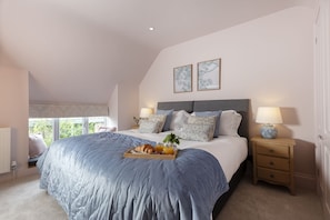 Une chambre à coucher avec un grand lit, des tables de chevet, une fenêtre et deux tableaux encadrés accrochés au mur.