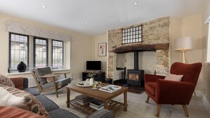 A cozy living room with a stone fireplace, a comfortable sofa, a red armchair, and a television. - Sun Cottage - Wonderful dog friendly cottage (Kingham)