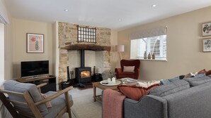 A cozy living room with a stone fireplace, a television, a sofa, and a comfortable chair. - Sun Cottage - Wonderful dog friendly cottage (Kingham)