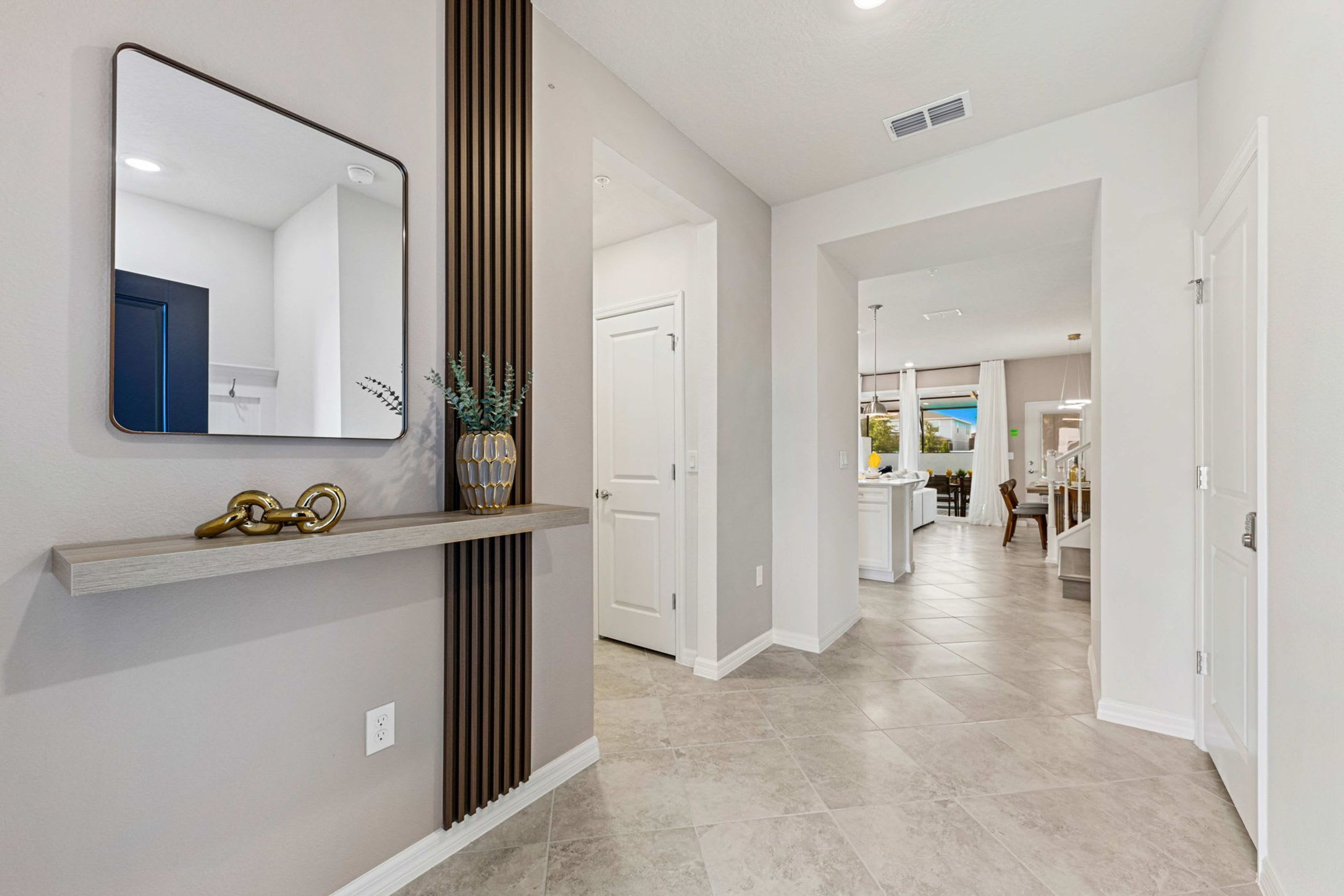 A hallway with a mirror, a shelf with decorative items, and a door leading to another room.