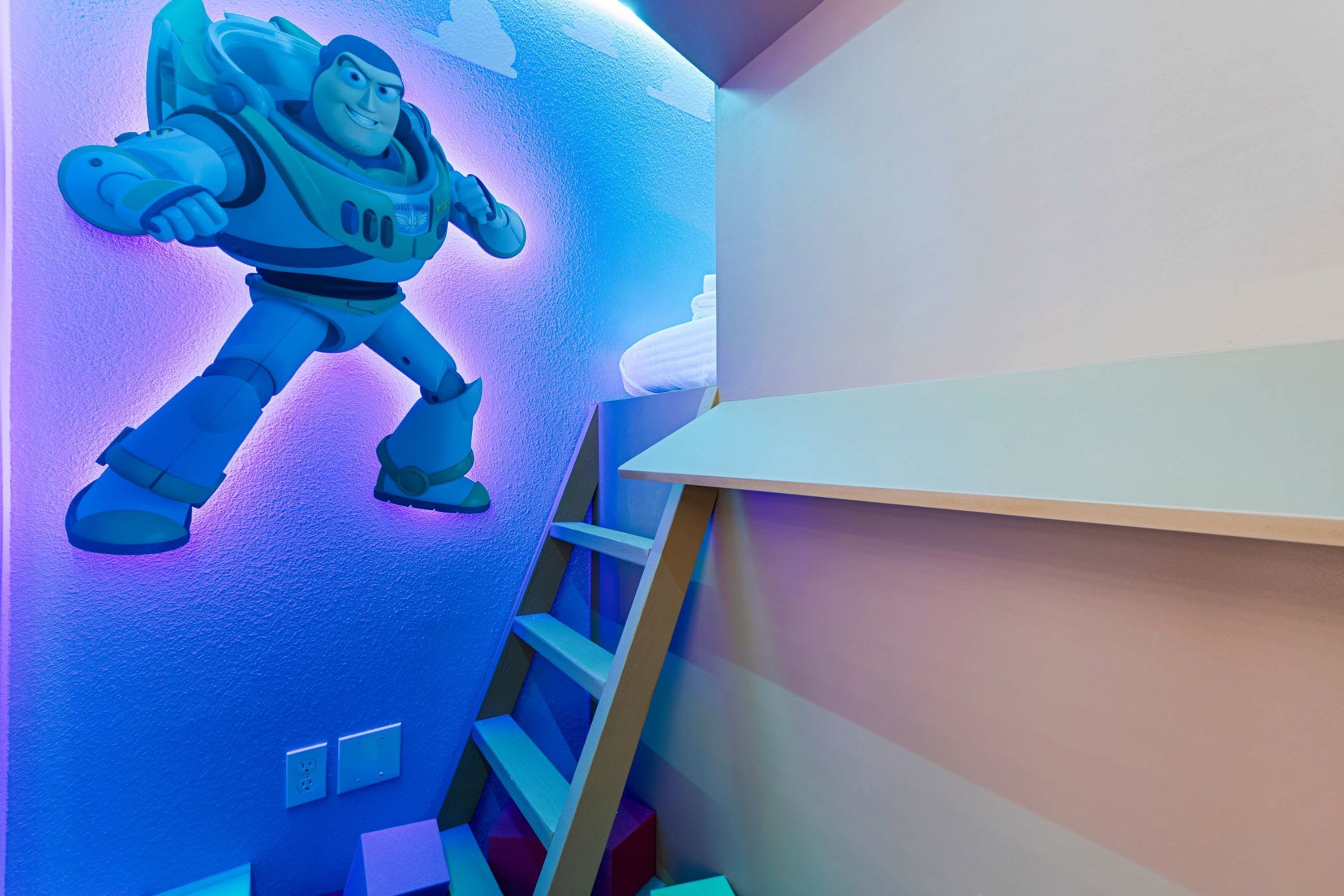 Een kamer met een aan de muur bevestigde astronautenfiguur, een houten ladder en een witte plank.