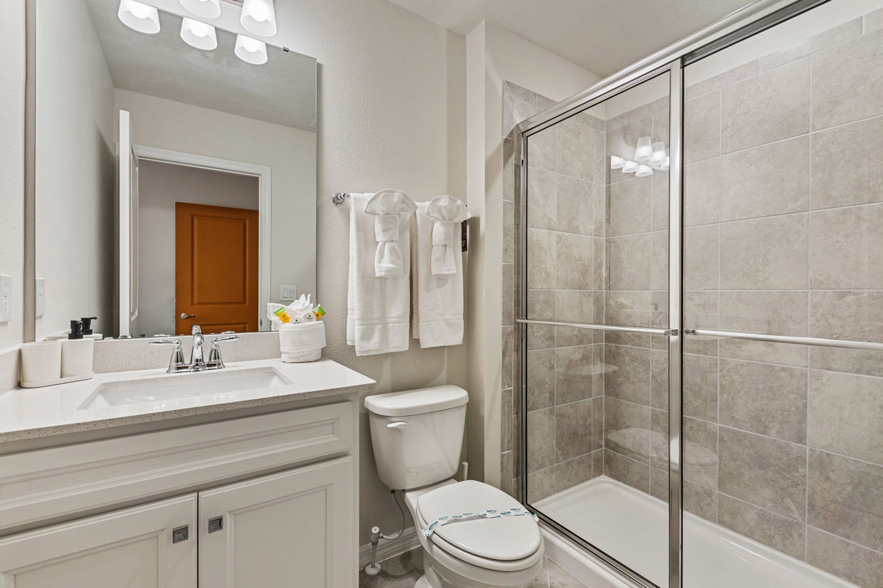 A bathroom with a shower, toilet, sink, and a mirror.