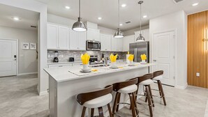 A modern kitchen with white cabinets, stainless steel appliances, and a central island with bar stools. - 5BR w Pool Grill Game Lounge Indoor Slide 16165 (Clermont)