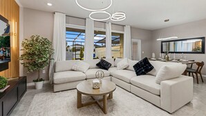 A modern living room with a sectional sofa, a round coffee table, and pendant lighting. - 5BR w Pool Grill Game Lounge Indoor Slide 16165 (Clermont)