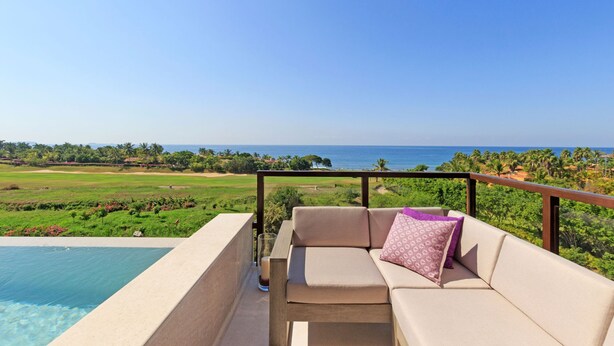 Ein Balkon mit einer Couch und einem Getränk, mit Blick auf einen Golfplatz und das Meer.