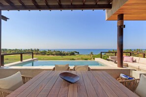 A wooden table with a cushion, a wicker chair, and a view of a pool and ocean. - Condo Argo in Punta Mita (Punta de Mita)