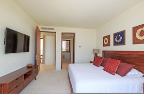 A bedroom with a large bed, a TV, a wooden dresser, and a bathroom visible through an open door. - Condo Argo in Punta Mita (Punta de Mita)