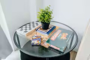 Taula de vidre amb una planta en test, un tauler d'escacs, alguns llibres i un paquet de menjar.