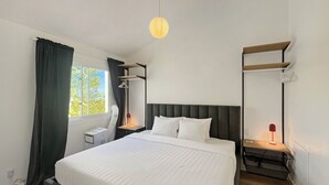 A hotel room with a large bed, bedside tables, a desk, a chair, a hanging light fixture, and a window with curtains.